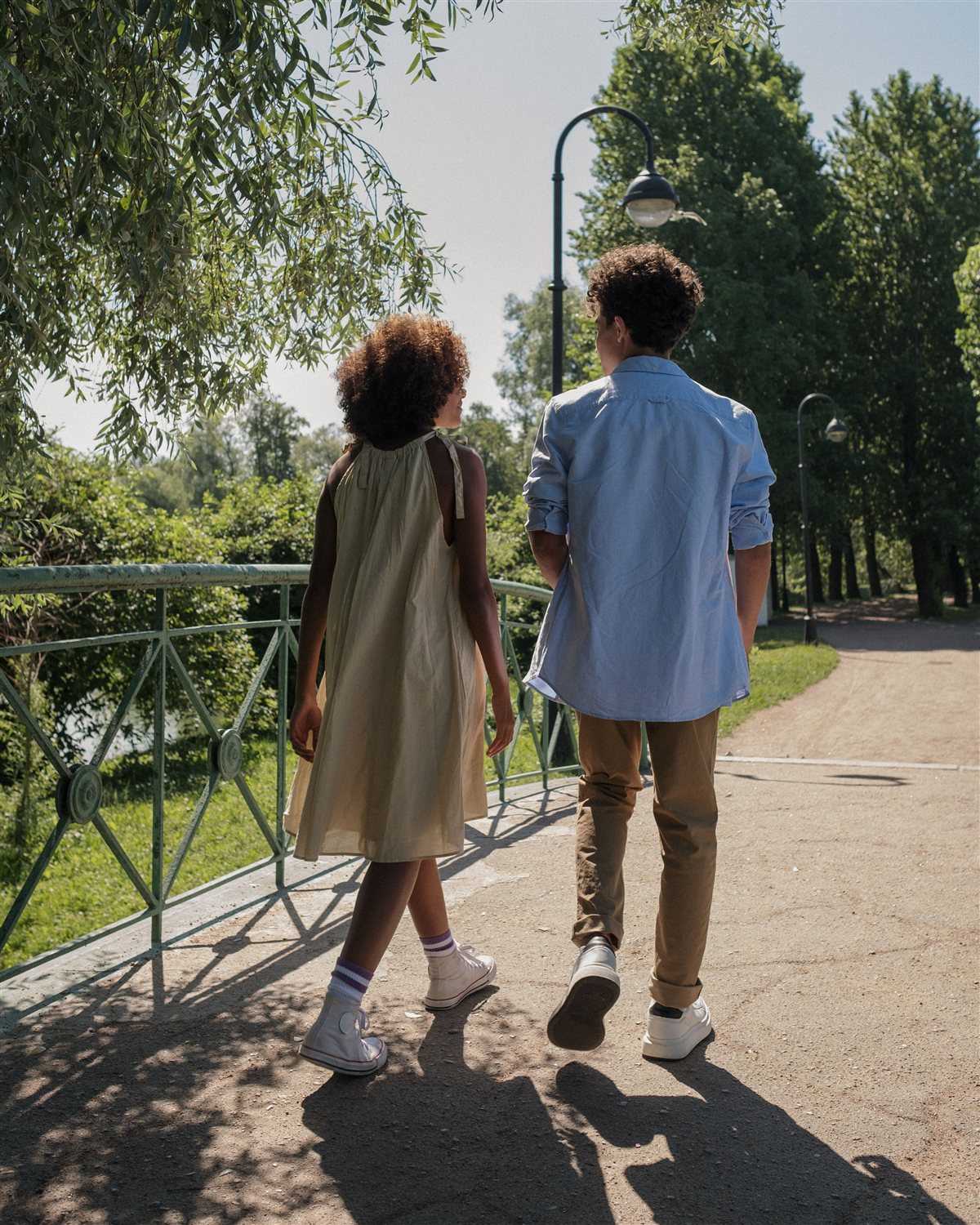 Simran and Krunal walking and talking together outdoors on a tree-lined path