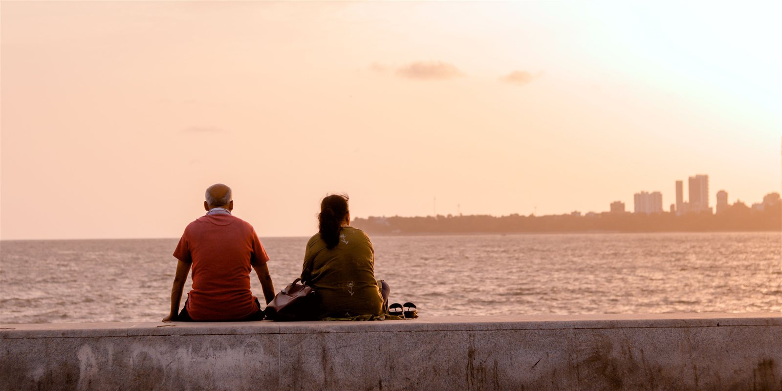 Two people sitting together at the water's edge, looking out at the ocean at sunset